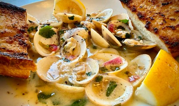 Steamed clams open in a lemon-garlic broth with parsley and grilled garlic bread.